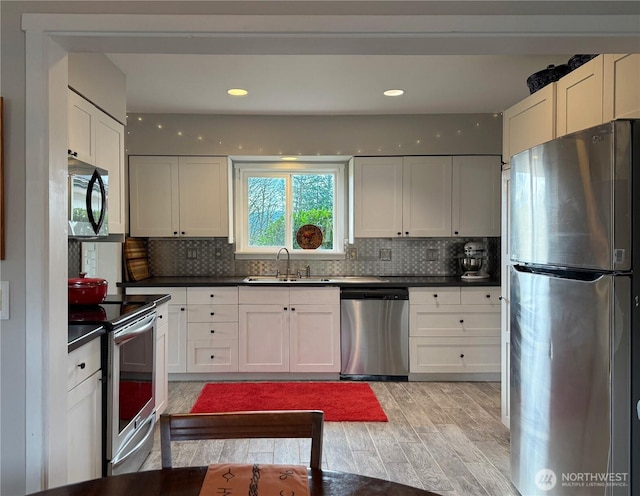 kitchen with appliances with stainless steel finishes, dark countertops, white cabinetry, and a sink