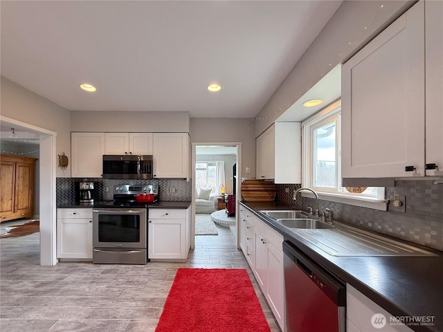 kitchen featuring stainless steel appliances, a sink, white cabinetry, a wealth of natural light, and dark countertops