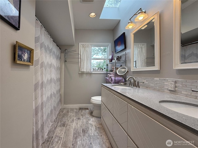 full bathroom with toilet, a skylight, double vanity, and a sink