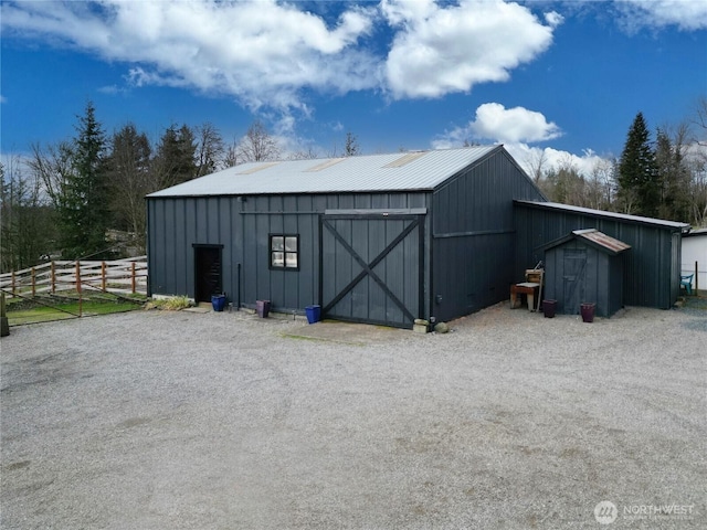 view of outdoor structure with gravel driveway, fence, and an outbuilding