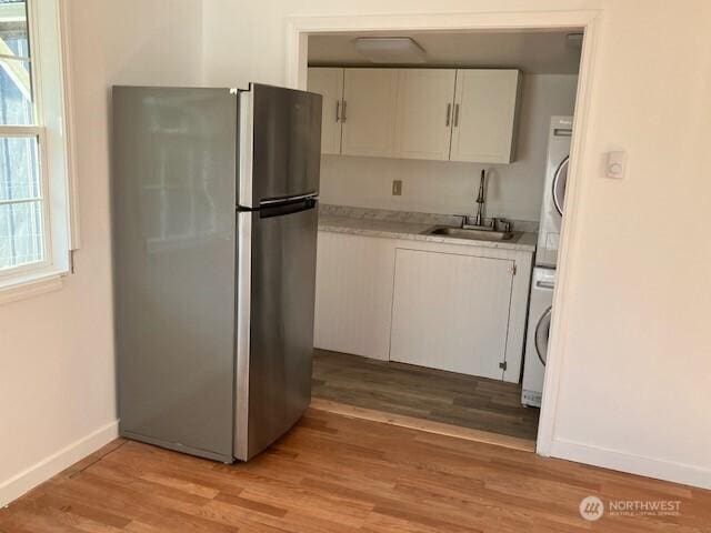 kitchen featuring light countertops, freestanding refrigerator, stacked washer / dryer, white cabinetry, and a sink