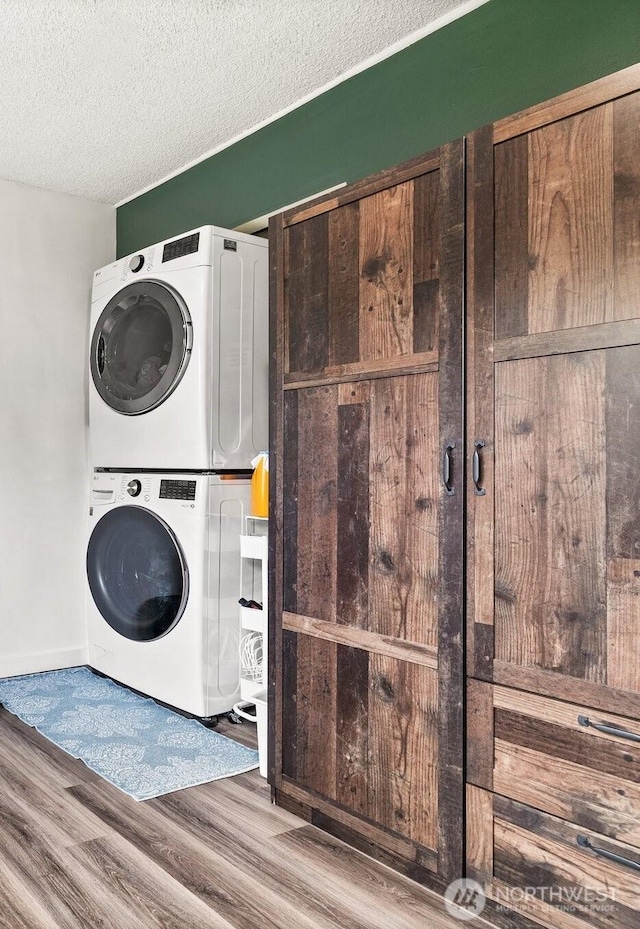 laundry area featuring a textured ceiling, baseboards, stacked washer and dryer, and wood finished floors