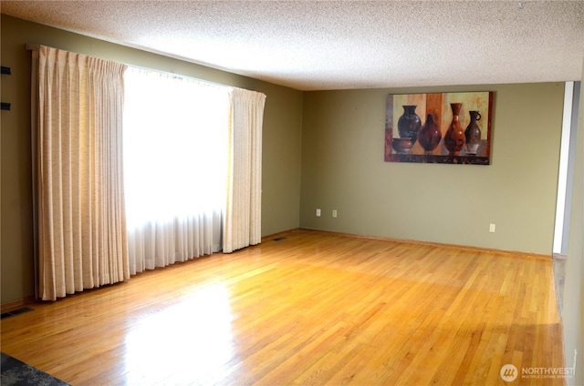 empty room with a textured ceiling, visible vents, and wood finished floors