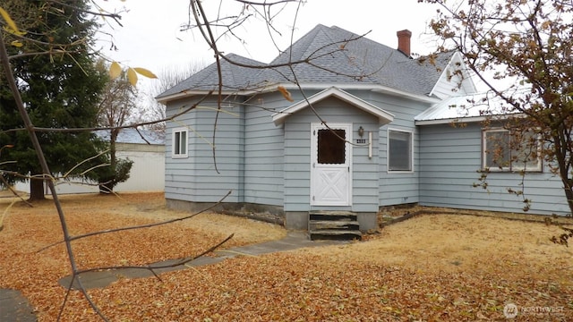 back of property featuring entry steps, roof with shingles, and a chimney