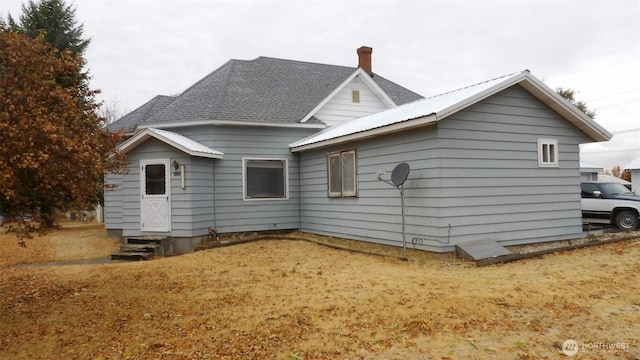 back of property with entry steps, a shingled roof, a chimney, and metal roof