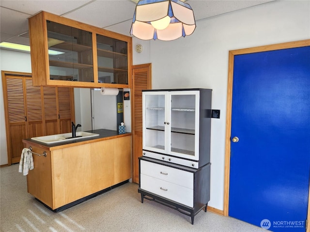 kitchen featuring glass insert cabinets, a paneled ceiling, a sink, and dark countertops