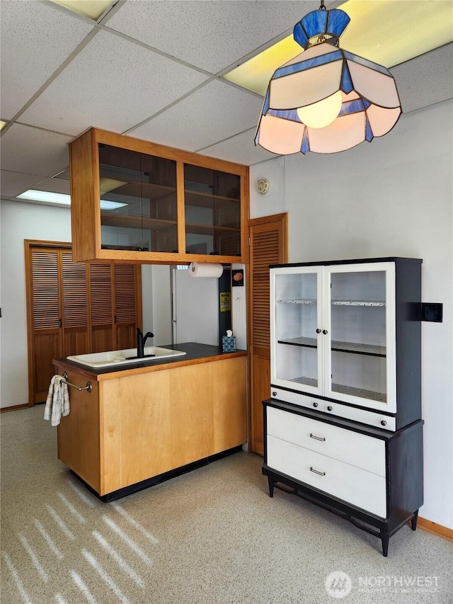 kitchen featuring a paneled ceiling, a peninsula, baseboards, and a sink