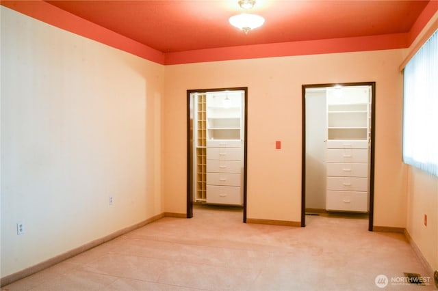 unfurnished bedroom featuring light carpet, baseboards, and multiple closets