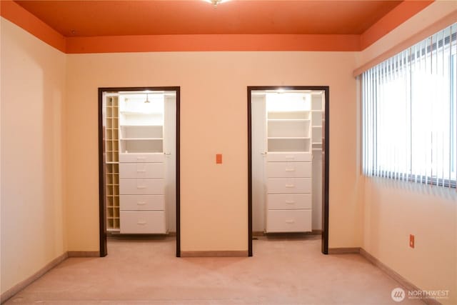 unfurnished bedroom featuring light carpet, baseboards, a walk in closet, and a closet