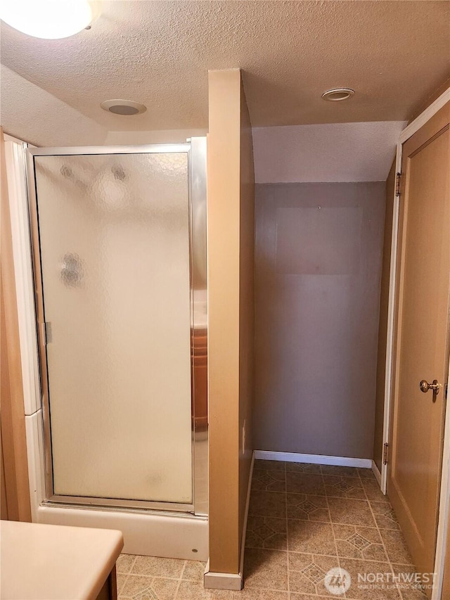 full bathroom featuring a shower stall, baseboards, and a textured ceiling