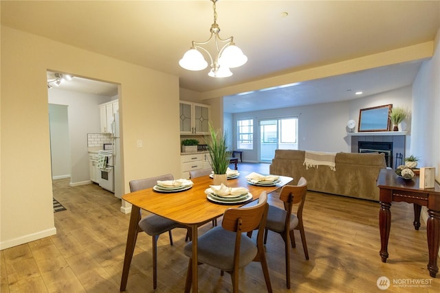 dining room featuring light wood-style floors, baseboards, a notable chandelier, and a tiled fireplace