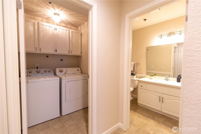 clothes washing area featuring a textured wall, a sink, cabinet space, and washer and dryer