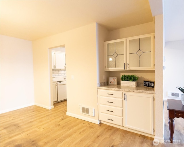 bar with white dishwasher, visible vents, baseboards, backsplash, and light wood finished floors