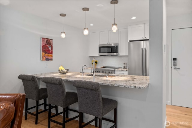 kitchen featuring light stone counters, a breakfast bar, stainless steel appliances, light wood-type flooring, and white cabinetry