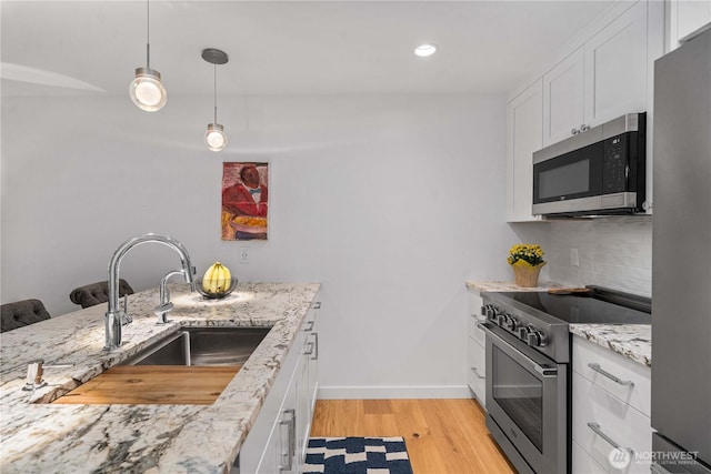 kitchen featuring a sink, white cabinetry, appliances with stainless steel finishes, light wood-type flooring, and backsplash