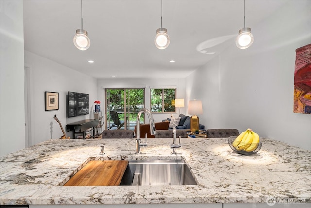 kitchen featuring light stone counters, recessed lighting, a sink, open floor plan, and decorative light fixtures