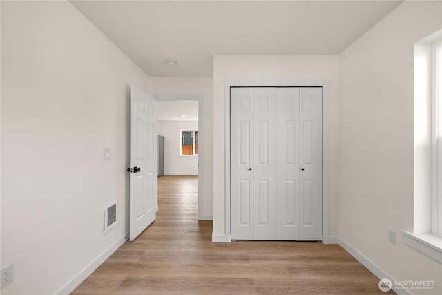 unfurnished bedroom with light wood finished floors, baseboards, visible vents, and a closet