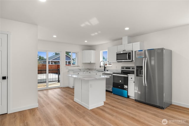 kitchen featuring a center island, stainless steel appliances, light countertops, light wood-style floors, and white cabinetry