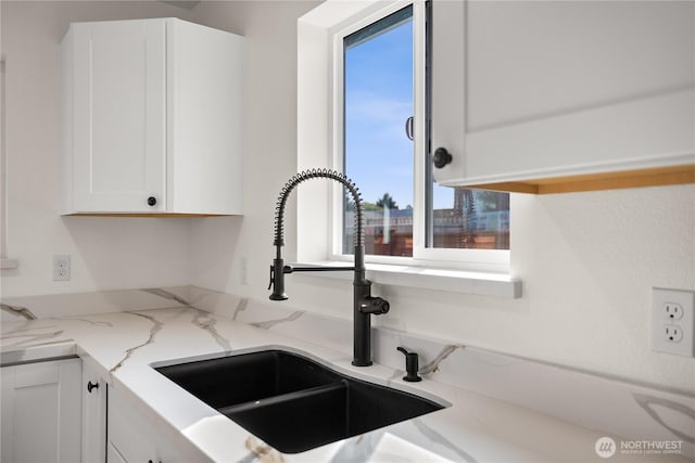 interior details with white cabinets, a sink, and light stone countertops