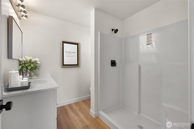 bathroom featuring wood finished floors, a shower stall, vanity, and baseboards