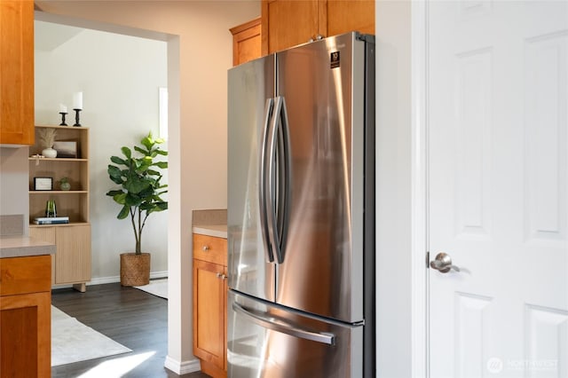 kitchen featuring brown cabinetry, light countertops, dark wood-style flooring, and freestanding refrigerator