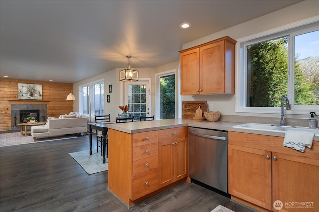 kitchen featuring a glass covered fireplace, a peninsula, light countertops, stainless steel dishwasher, and a sink