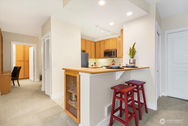 kitchen with light carpet, baseboards, a breakfast bar area, and stainless steel appliances