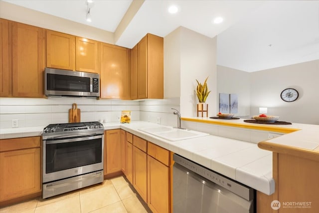 kitchen with light tile patterned floors, stainless steel appliances, backsplash, a sink, and a peninsula