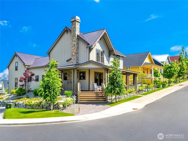 view of front of home with metal roof, covered porch, a residential view, board and batten siding, and a chimney