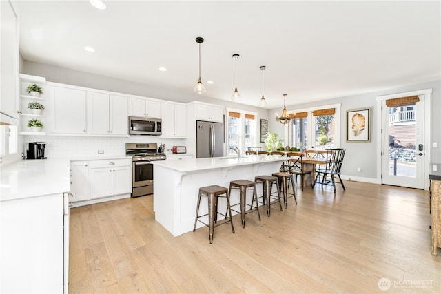 kitchen with a center island with sink, light wood-style flooring, appliances with stainless steel finishes, open shelves, and backsplash