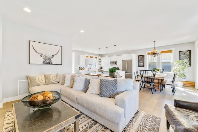 living room featuring baseboards, visible vents, light wood-type flooring, a chandelier, and recessed lighting