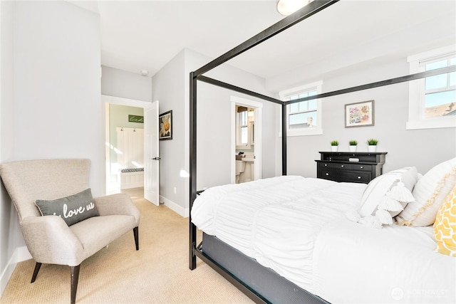 bedroom with light colored carpet, baseboards, multiple windows, and ensuite bath