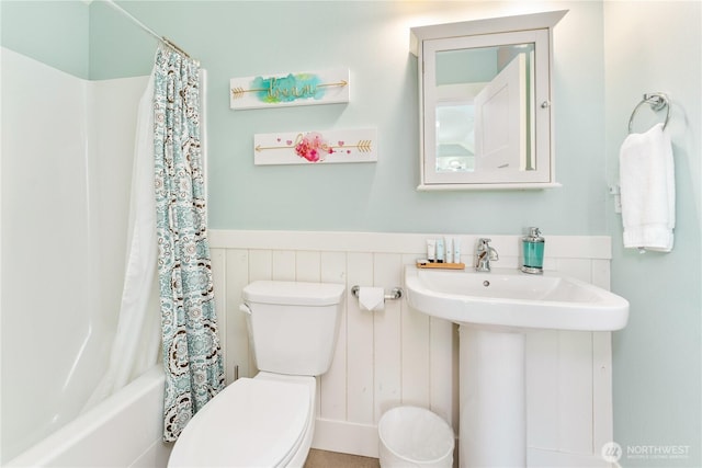 bathroom with a sink, wainscoting, shower / bath combo with shower curtain, and toilet