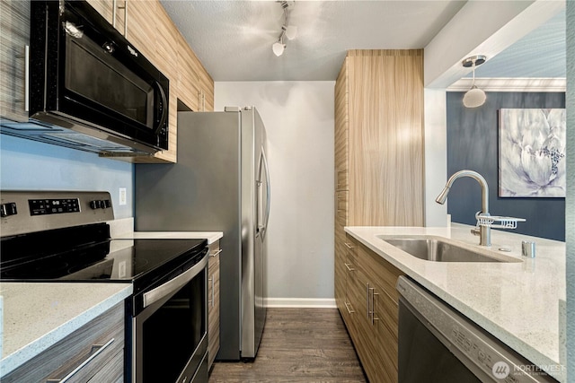 kitchen featuring light stone counters, stainless steel appliances, a sink, baseboards, and dark wood finished floors