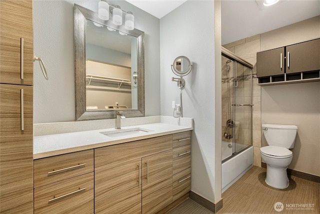 bathroom with toilet, baseboards, combined bath / shower with glass door, and vanity