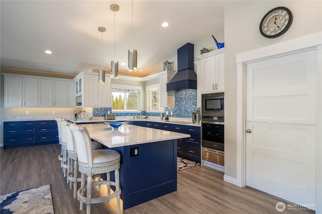 kitchen featuring a center island, premium range hood, black appliances, a warming drawer, and a sink