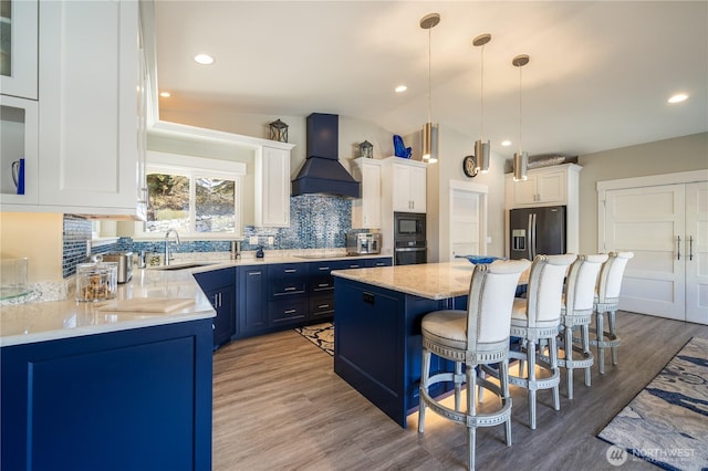 kitchen featuring a breakfast bar, a sink, custom range hood, stainless steel refrigerator with ice dispenser, and a center island