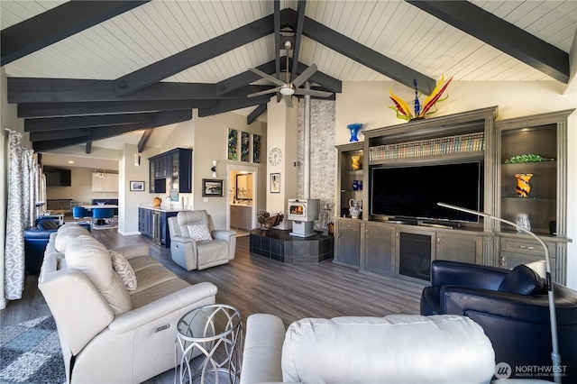 living room featuring beam ceiling, a wood stove, wood finished floors, and ceiling fan