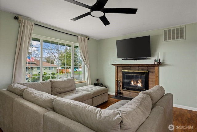 living room featuring a brick fireplace, visible vents, baseboards, and wood finished floors