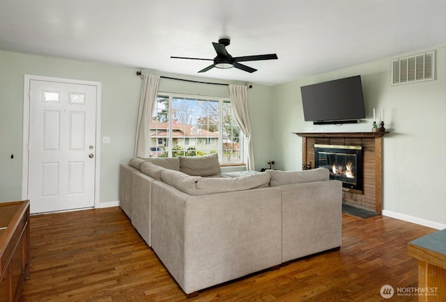 living room featuring ceiling fan, wood finished floors, visible vents, baseboards, and a brick fireplace