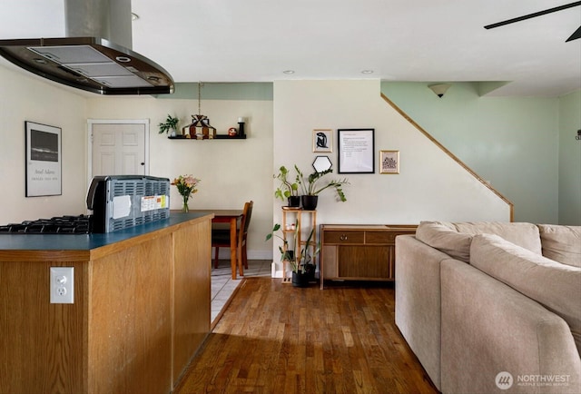 kitchen with island range hood, a ceiling fan, brown cabinets, dark countertops, and dark wood finished floors