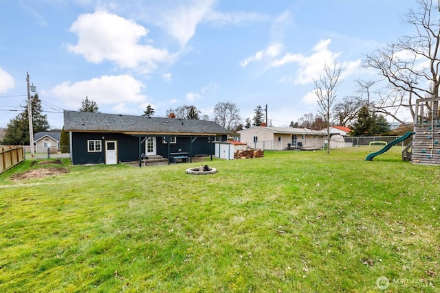 exterior space with an outdoor fire pit, a playground, a lawn, and a fenced backyard