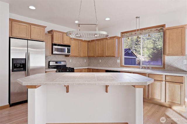 kitchen featuring light wood finished floors, a kitchen island, a breakfast bar area, decorative backsplash, and stainless steel appliances