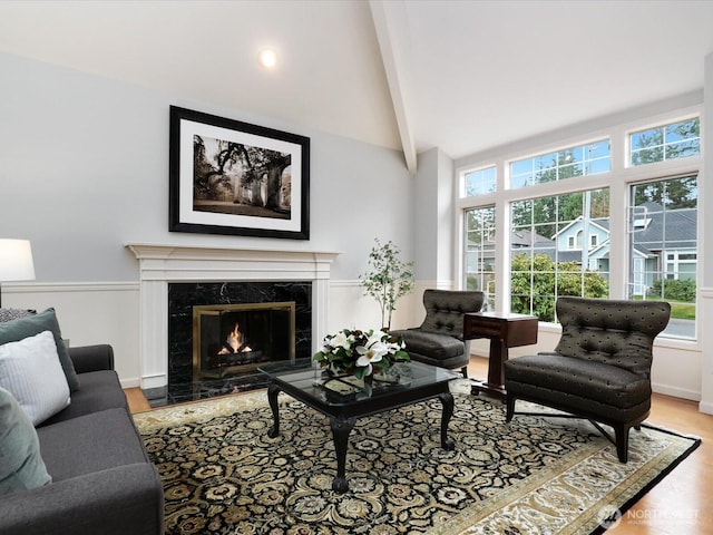 living area with high vaulted ceiling, a high end fireplace, and light wood-style flooring