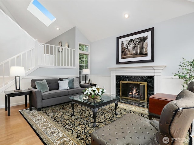 living area featuring a skylight, stairway, a premium fireplace, wood finished floors, and high vaulted ceiling