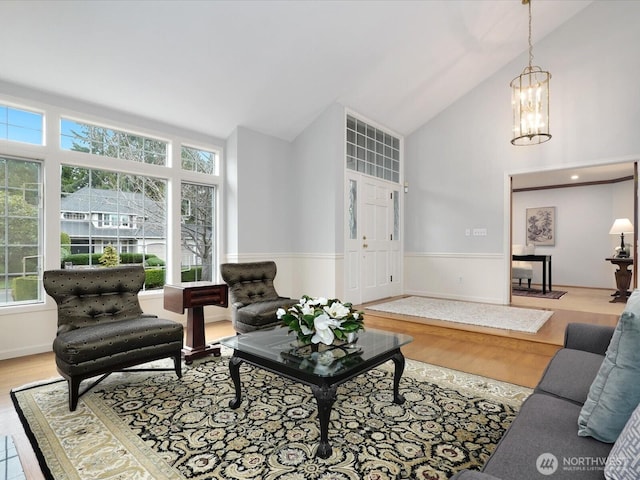 living area with high vaulted ceiling, wainscoting, wood finished floors, and an inviting chandelier