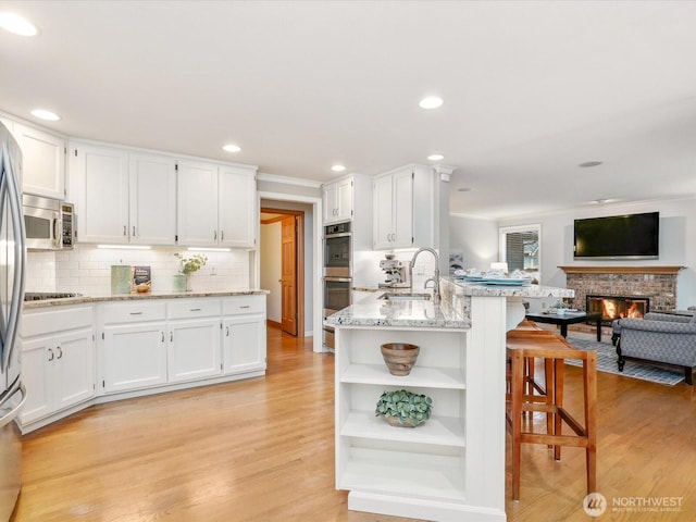 kitchen featuring open shelves, appliances with stainless steel finishes, white cabinetry, a sink, and a kitchen breakfast bar