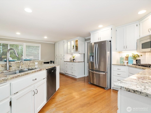 kitchen with light stone counters, a sink, white cabinetry, light wood-style floors, and appliances with stainless steel finishes