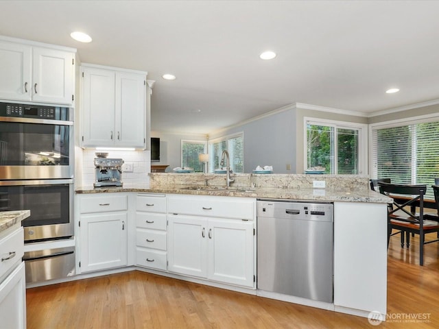 kitchen featuring a warming drawer, light wood finished floors, stainless steel appliances, white cabinets, and a sink