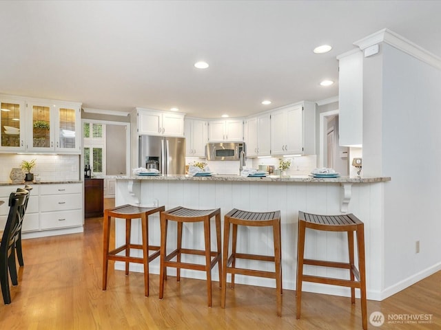 kitchen featuring stainless steel appliances, a peninsula, white cabinetry, and light wood-style floors